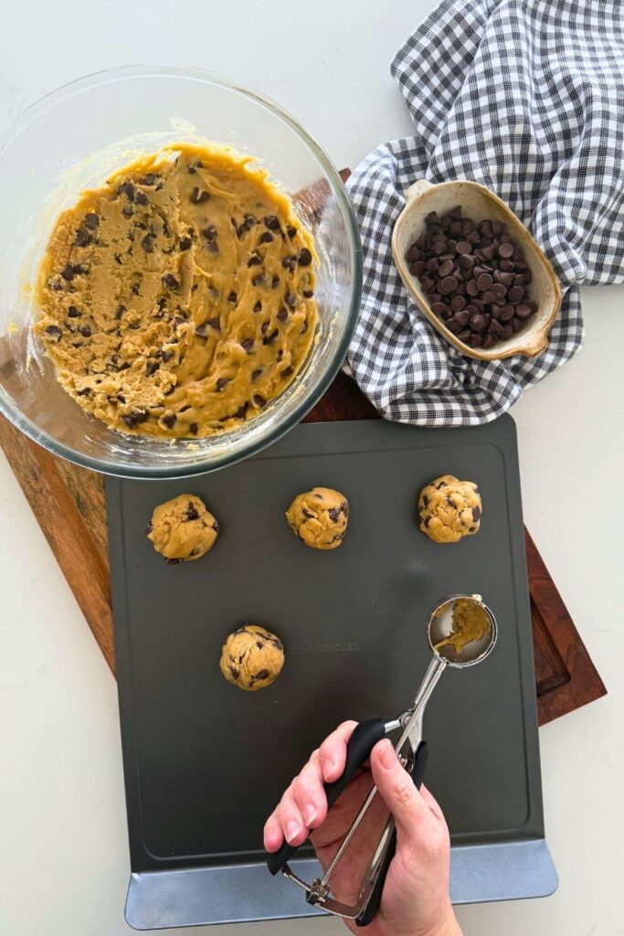 A tray of sourdough chocolate chip cookie dough balls with a 2 tablespoon cookie dough scoop in the photo.