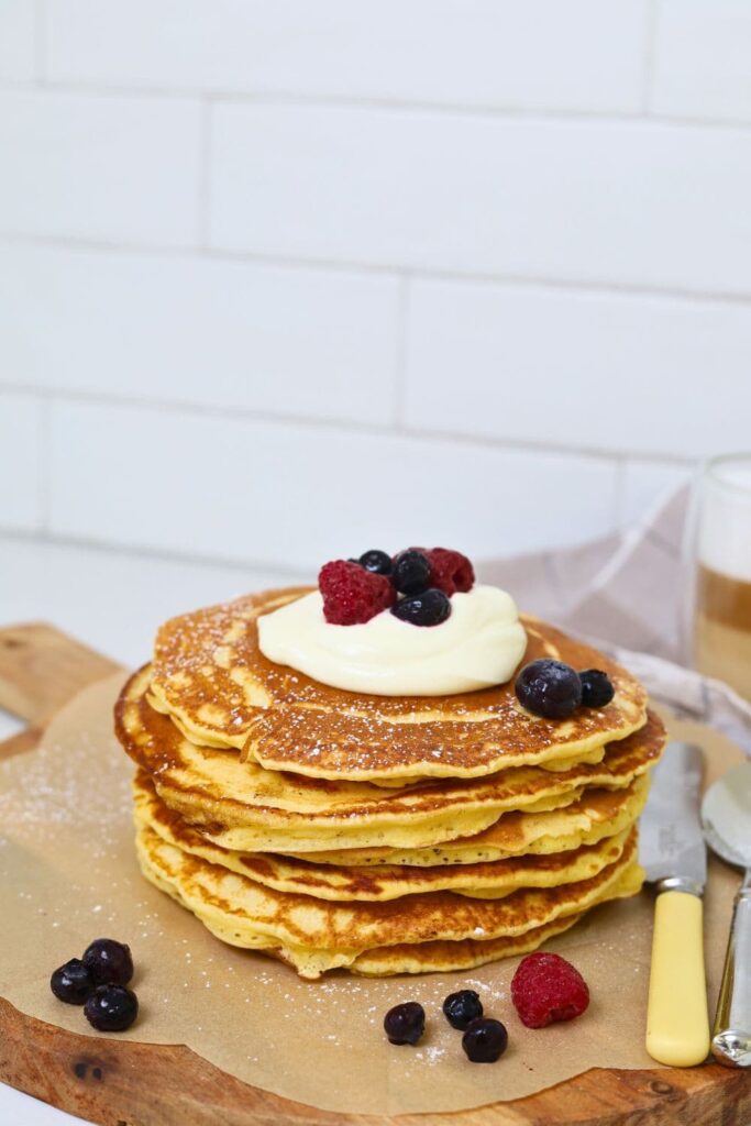 A stack of sourdough discard pancakes topped with whipped cream and berries and drizzled in maple syrup.