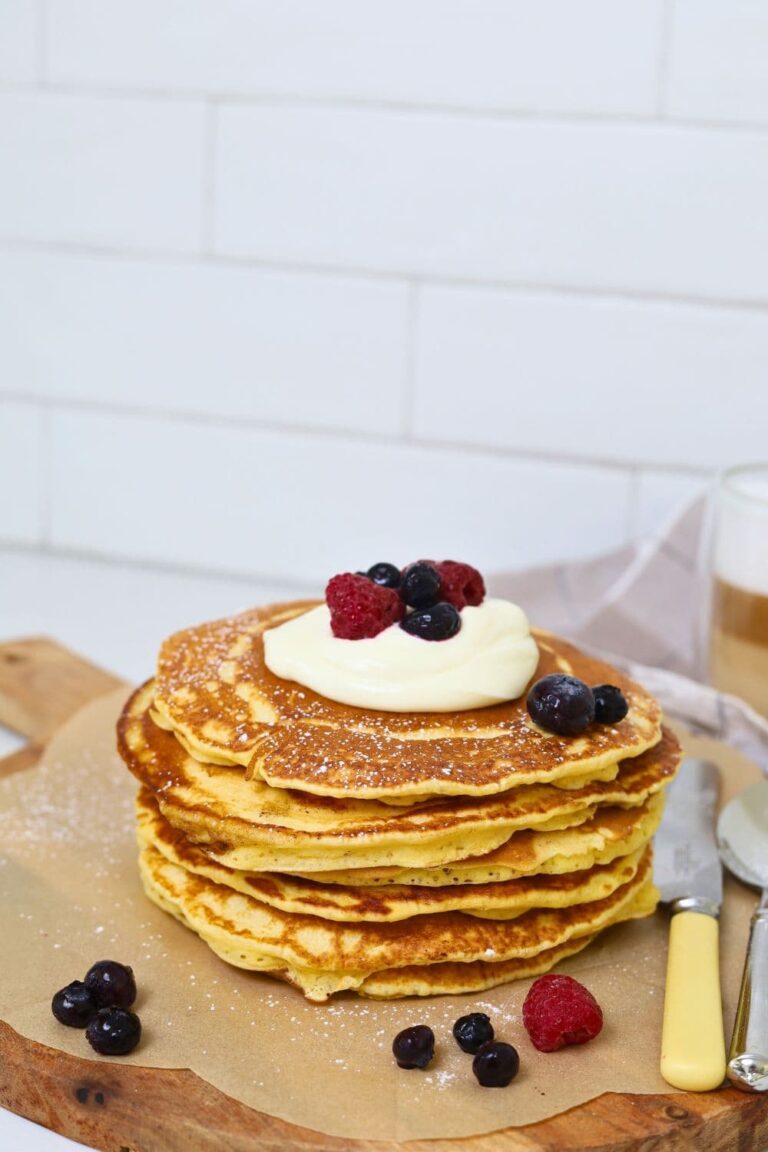 A stack of sourdough discard pancakes topped with whipped cream and berries and drizzled in maple syrup.