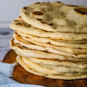 A stack of sourdough flatbreads on a round wooden board.