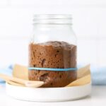A glass jar containing a chocolate sourdough starter. There is a blue rubber band on the jar showing that the chocolate sourdough starter has doubled.
