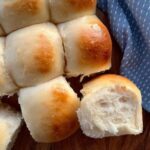 SOURDOUGH DINNER ROLLS ARRANGED WITH A BLUE DISH TOWEL. ONE HAS BEEN TURNED ON ITS SIDE SO YOU CAN SEE THE SOFT CRUMB.