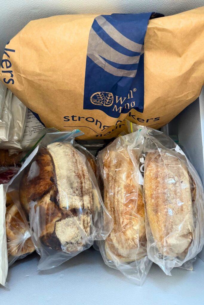 A photo of the inside of my freezer showing a large bag of flour and frozen sourdough loaves in ziplock bags.