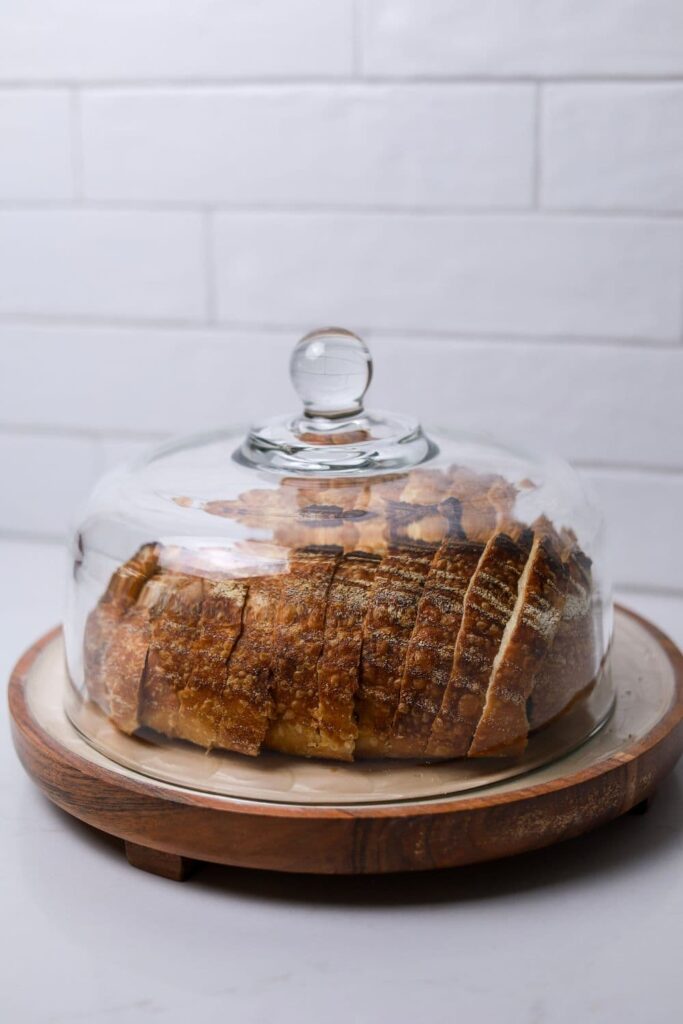 A sliced loaf of sourdough bread stored under a glass cloche.