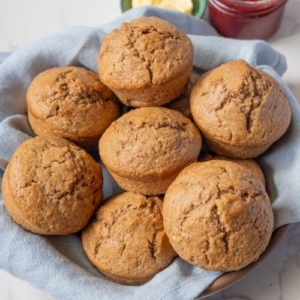 A batch of sourdough cinnamon muffins in a basket lined with a blue dish towel.