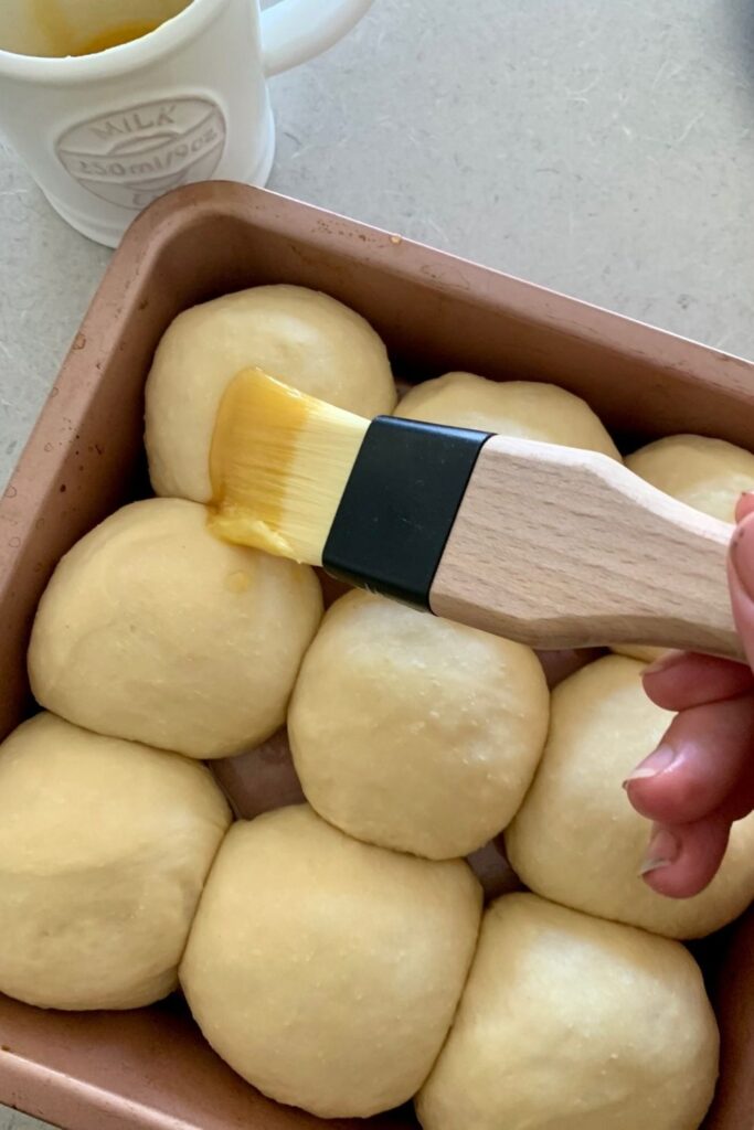 Sourdough Hawaiian rolls being brushed with melted butter before baking.