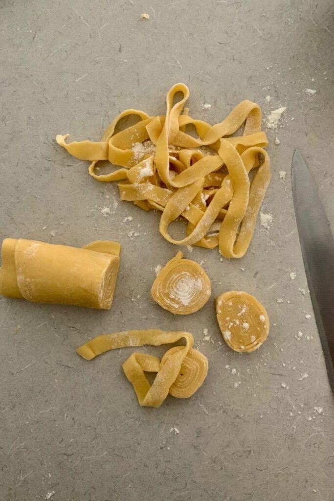 A photo showing the process of cutting sourdough pasta with a knife as opposed to using a pasta maker.