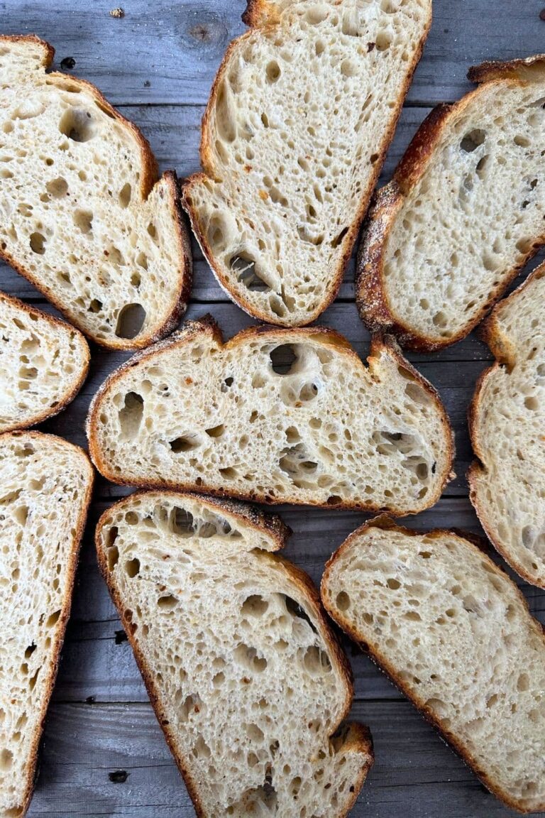 Slices of sourdough bread laid out on a wooden board so you can see the open, airy crumb inside and the deep golden crust on the outside.