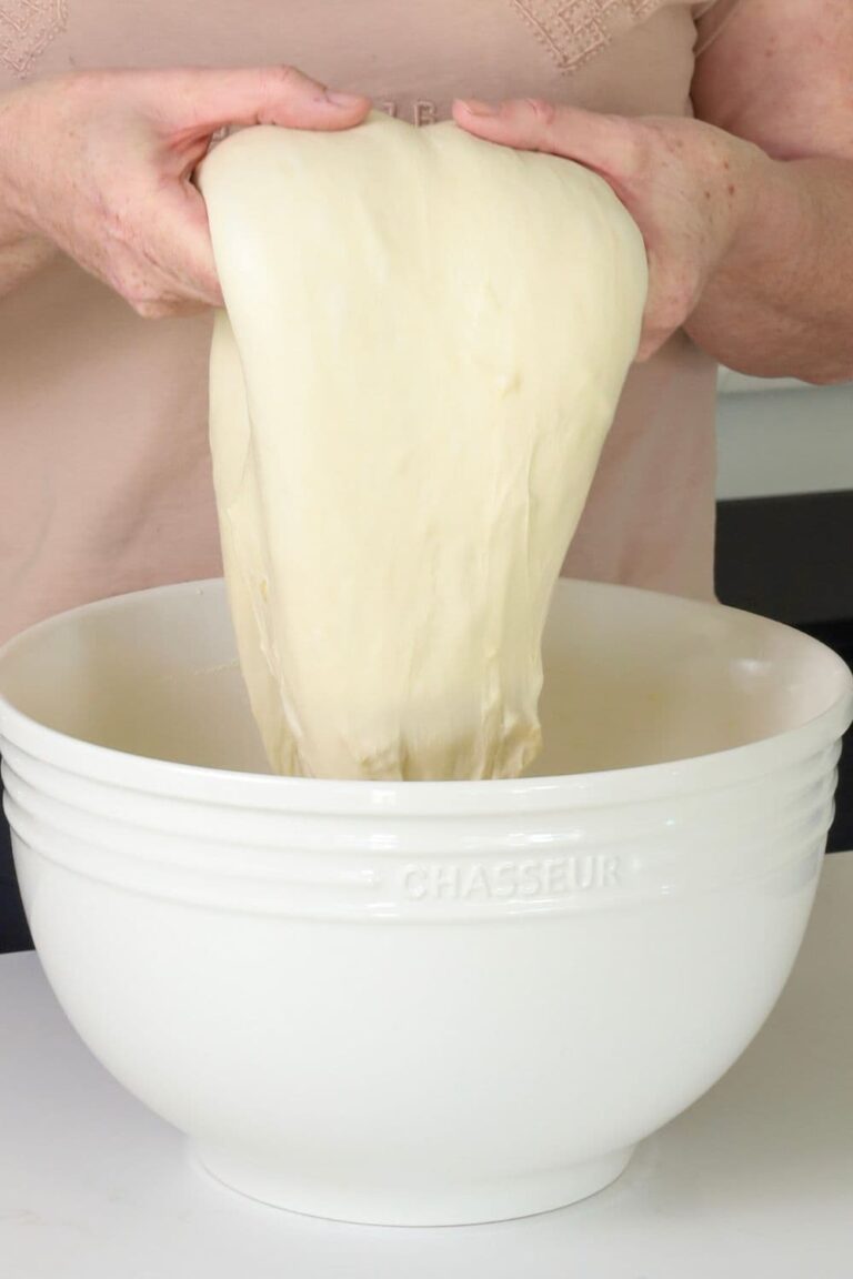 A photo showing a large cream colored bowl and someone performing coil folds on the dough out of the top of the bowl.