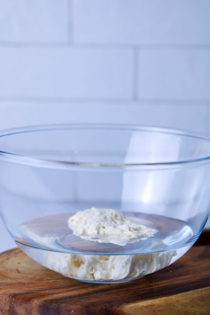 A large scoop of bubbly sourdough starter that has been added to a bowl of water to see whether it floats or not.
