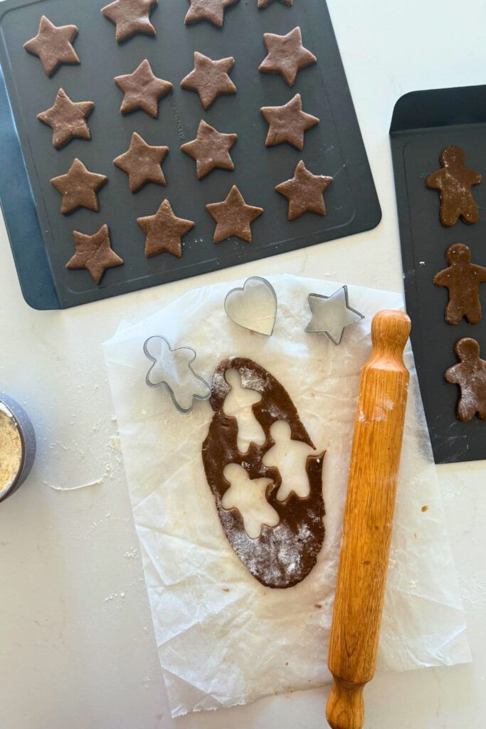 A small portion of sourdough gingerbread dough that has been rolled out and gingerbread men shapes have been cut out of the dough. There is also a tray of sourdough gingerbread cookie stars on a tray.