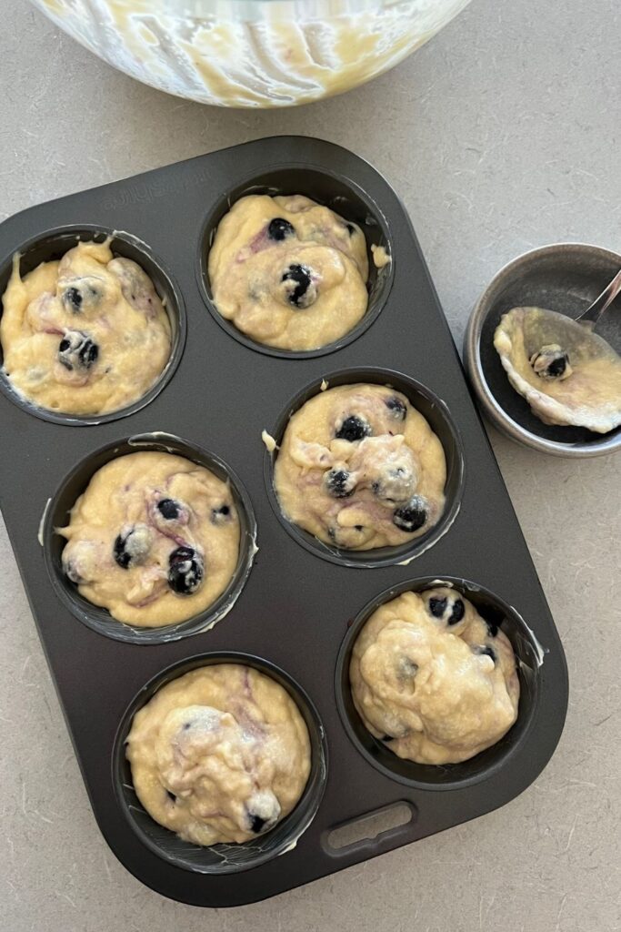 Overnight sourdough blueberry muffin mixture spooned into a 6 hole muffin tin.
