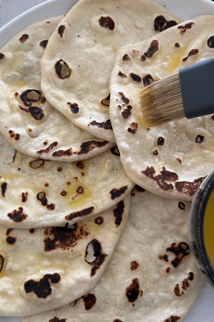 A plate of sourdough naan being brushed with melted butter.