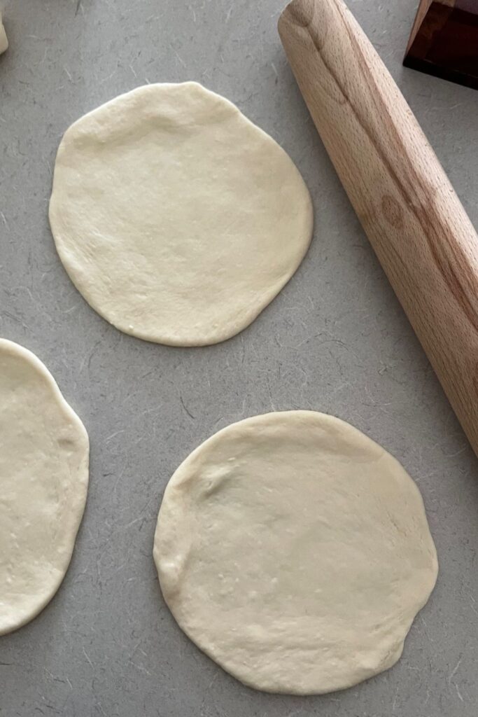 3 circles of dough rolled into sourdough naan bread. You can see a rolling pin the photo as well.