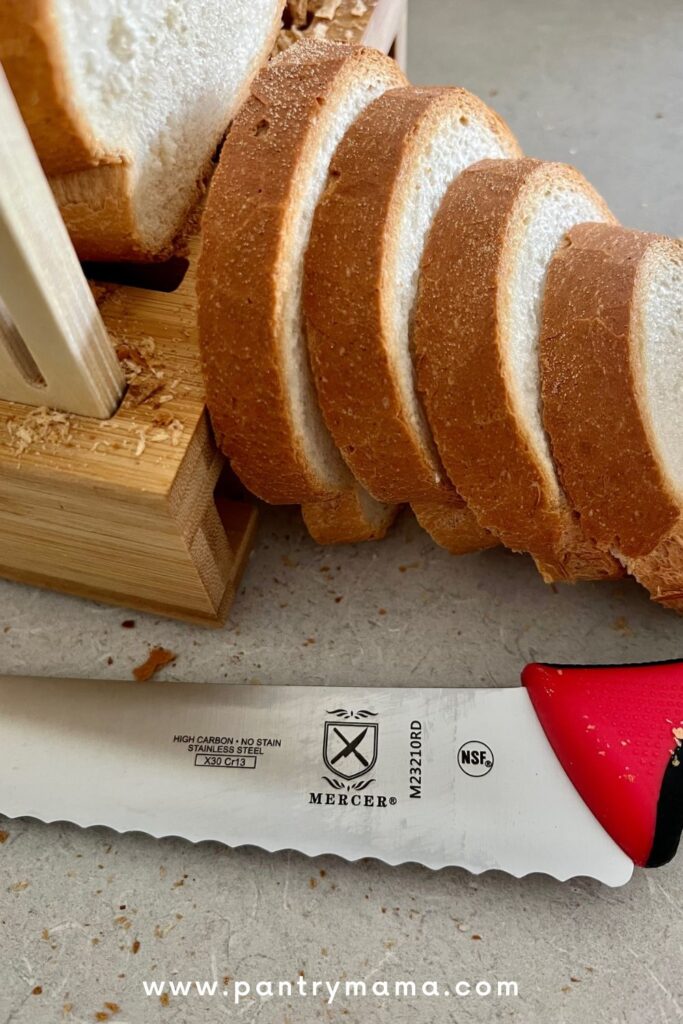 A Mercer bread knife sitting in front of a crusty loaf of bread.