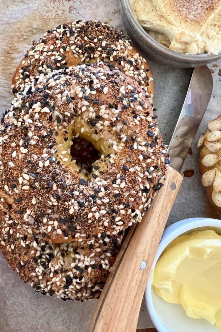 Homemade sourdough pumpkin bagels coated in homemade everything bagel seasoning. You an also see a small dish of butter and a butter knife in the photo.