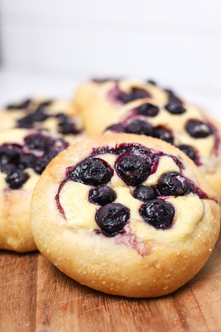 Close up photo of a sourdough brioche blueberry cheesecake roll that has just been baked. The blueberries are bleeding into the cheesecake filling.