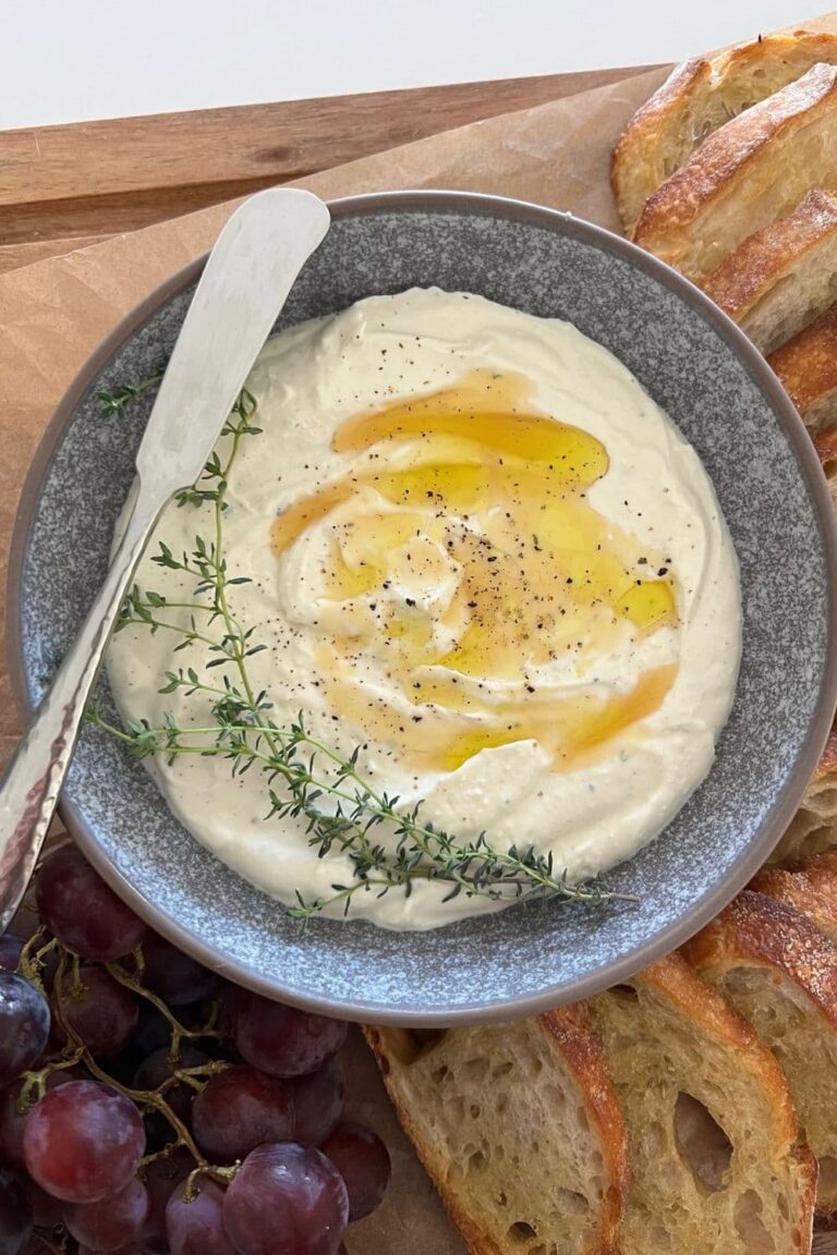 Whipped Ricotta Dip drizzled with honey and olive oil, dressed with fresh thyme leaves and served in a grey stoneware dish. There is a silver pate knife sitting on the edge of the bowl.