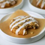 A sourdough oatmeal raisin cookie drizzled in a simple sugar glaze sitting on a piece of parchment paper on a small white plate.