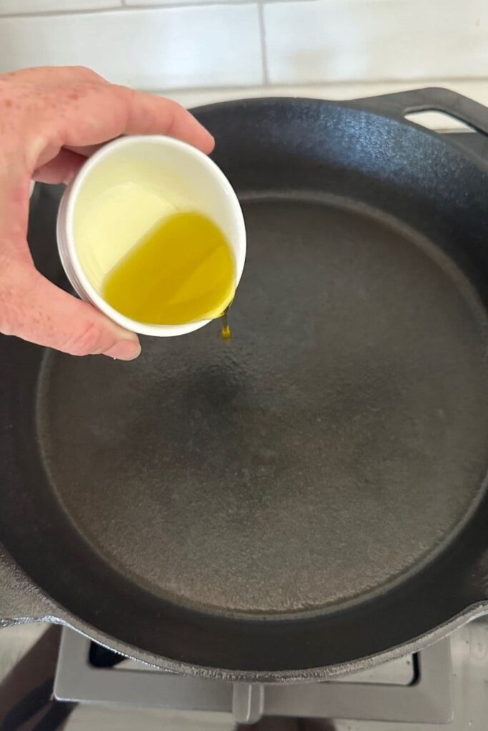 Olive oil being poured into a hot cast iron pan.