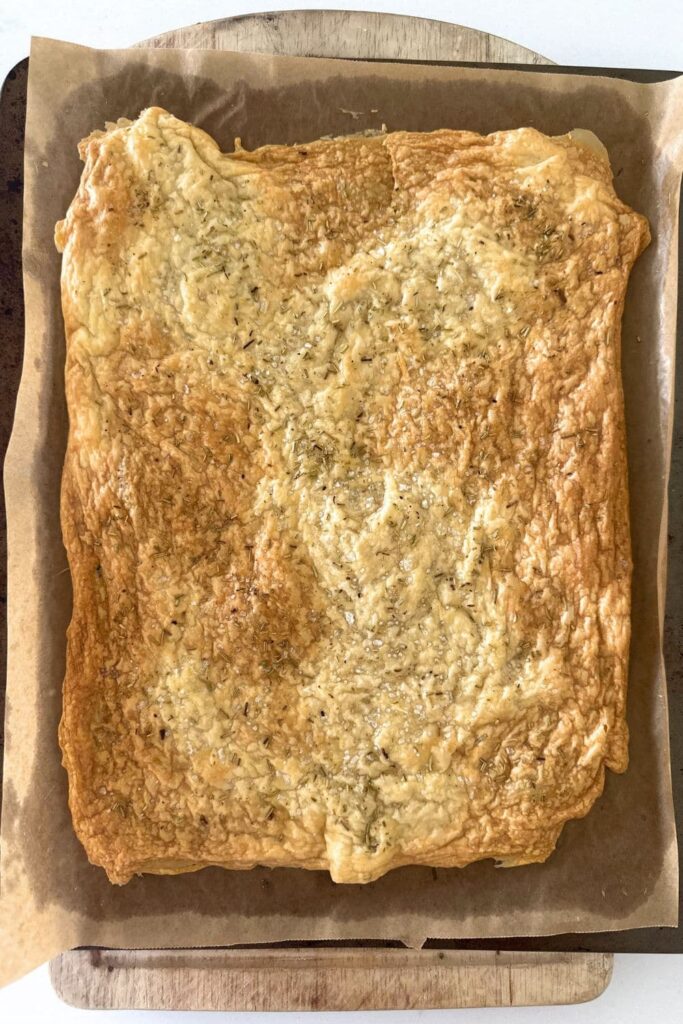 A photo showing a "sheet" of sourdough discard crackers that has been baked as a whole piece. It has been baked in the oven until golden brown and is sitting on a piece of parchment paper.