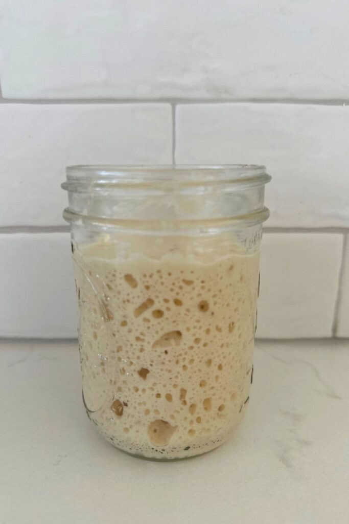 A mason jar without a lid filled with active, bubbly sourdough starter.