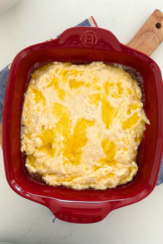 A red Emile Henry baking dish containing sourdough butter swim biscuit dough.
