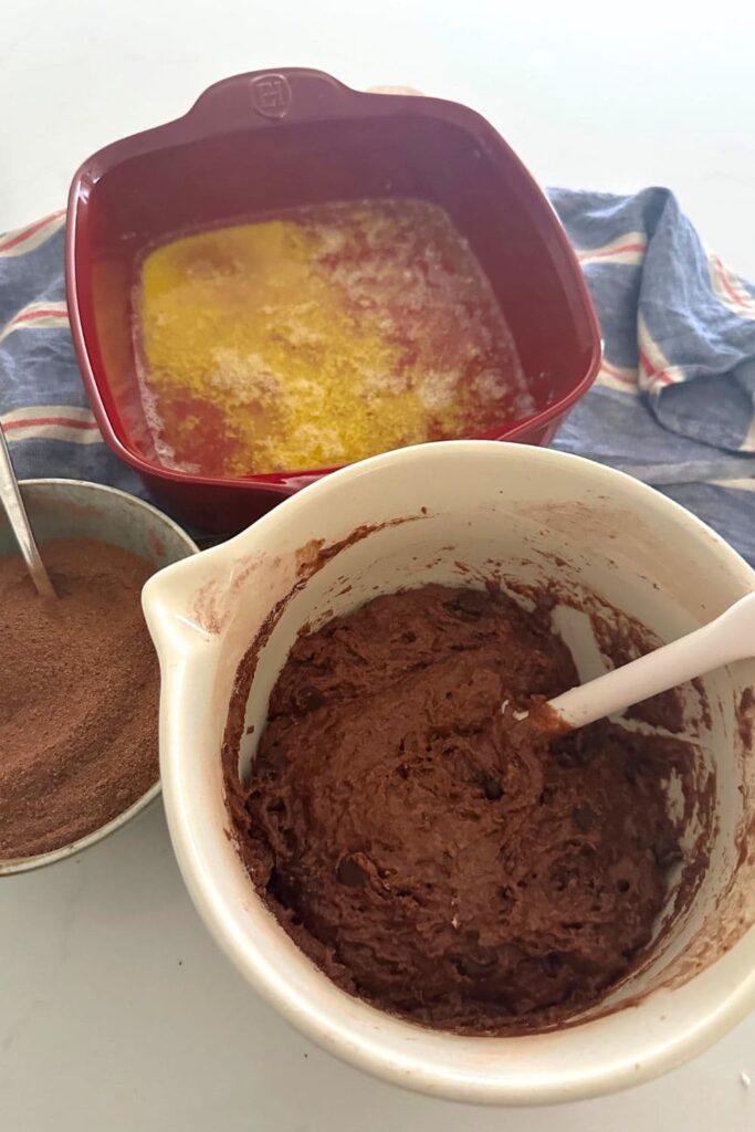 A batter jug containing batter for sourdough chocolate cobbler. In the background you can see a red Emile Henry dish filled with melted butter.