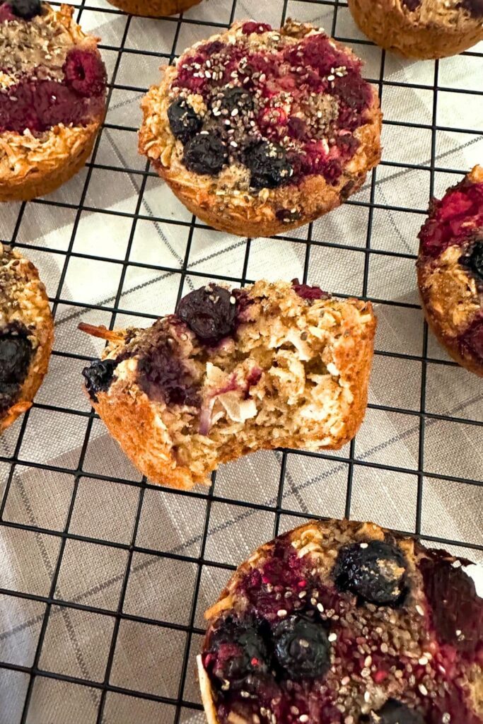 Sourdough oatmeal breakfast cups sitting on a wire rack. The one in the middle of the rack has a bite taken out so you can see the oatmeal crumb inside.