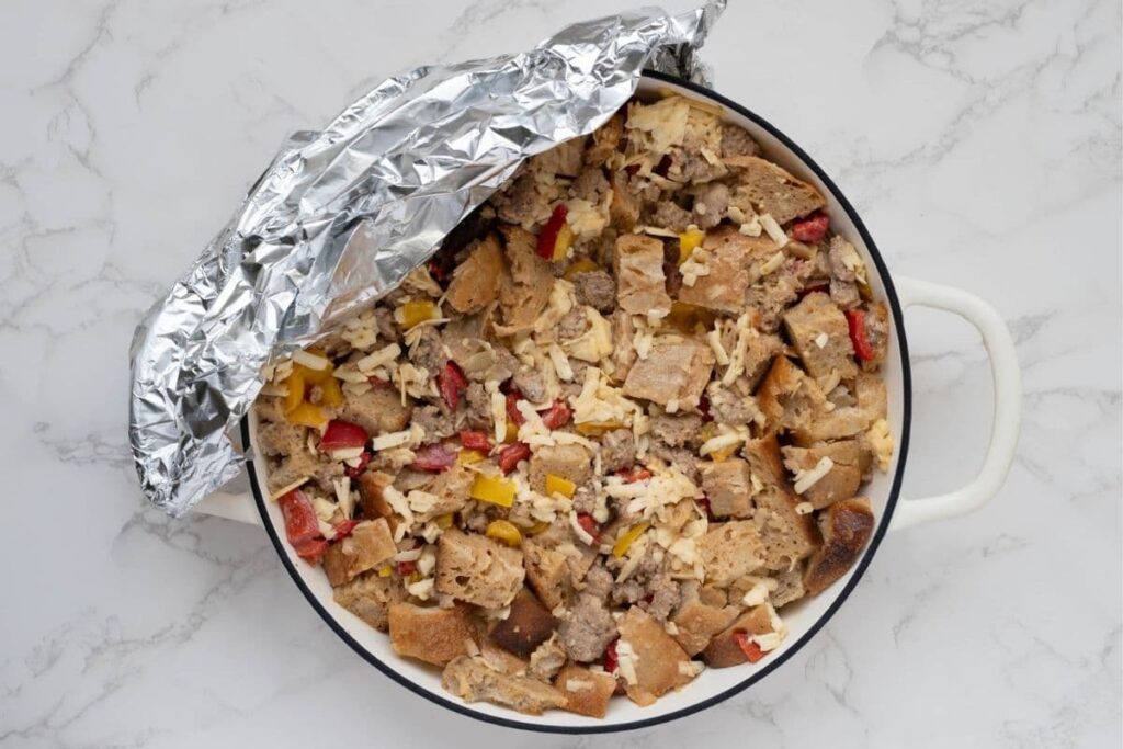 A round skillet of sourdough breakfast casserole that has been kept in the fridge overnight covered in aluminium foil.