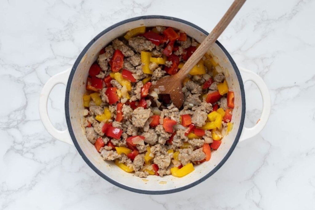 A white cast iron skillet filled with pork breakfast sausage and red and yellow bell peppers that have been cooked down.