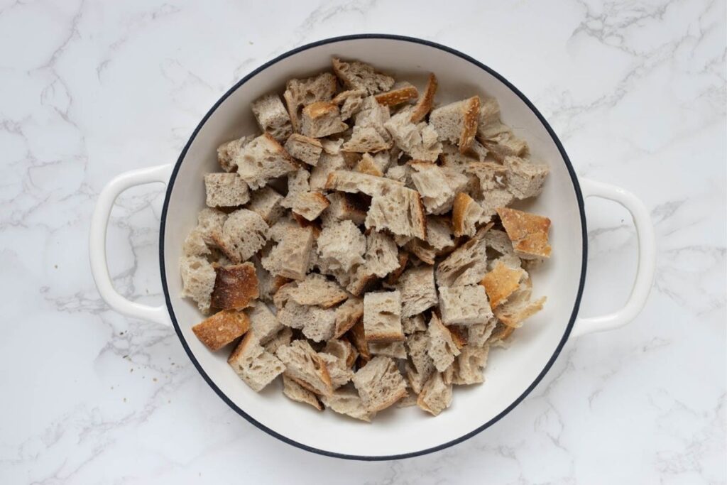 A white cast iron skillet filled with sourdough bread cubes.