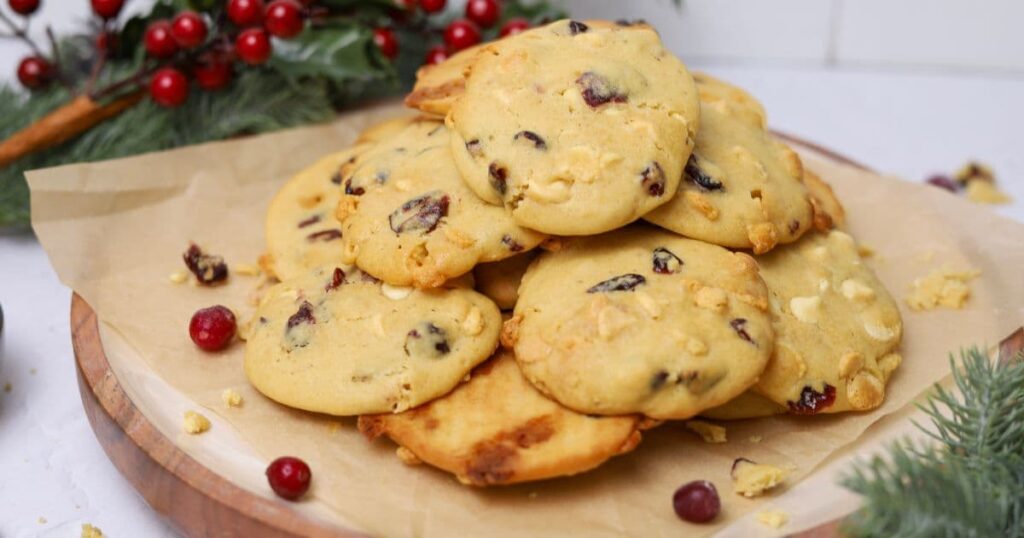 A pile of sourdough white chocolate cranberry cookies sitting on a round wooden platter.