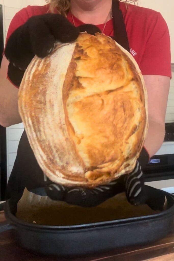 A loaf of sourdough croissant bread being held up just after being taken out of the oven.