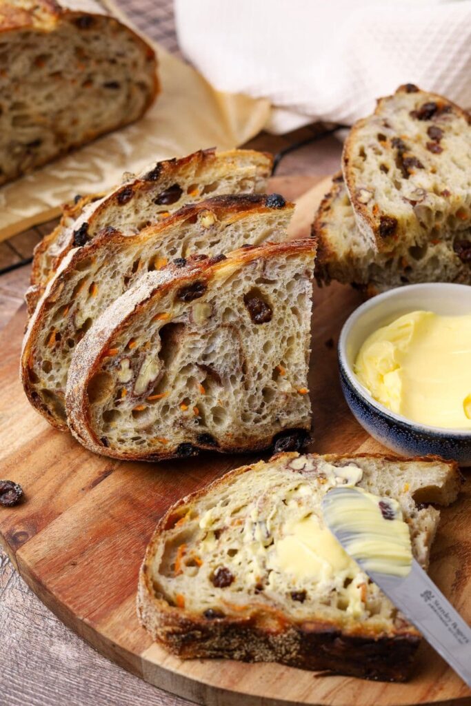 A loaf of sourdough carrot cake bread that has been sliced and buttered.