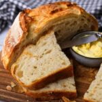 A loaf of sourdough croissant bread that has been sliced and served with a small bowl of butter.