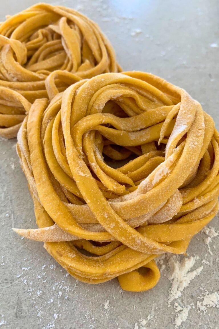 A nest of homemade sourdough pasta sitting on a floured counter top,.