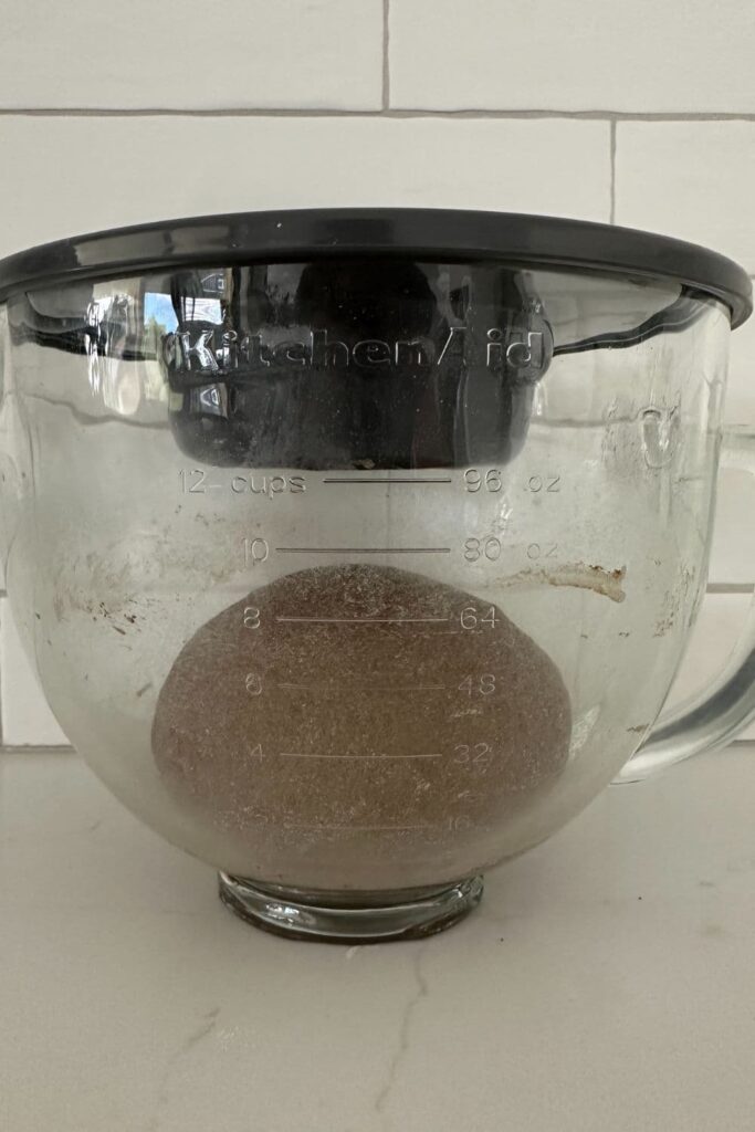 Sourdough brown bread rising during bulk fermentation in a glass KitchenAid jug.
