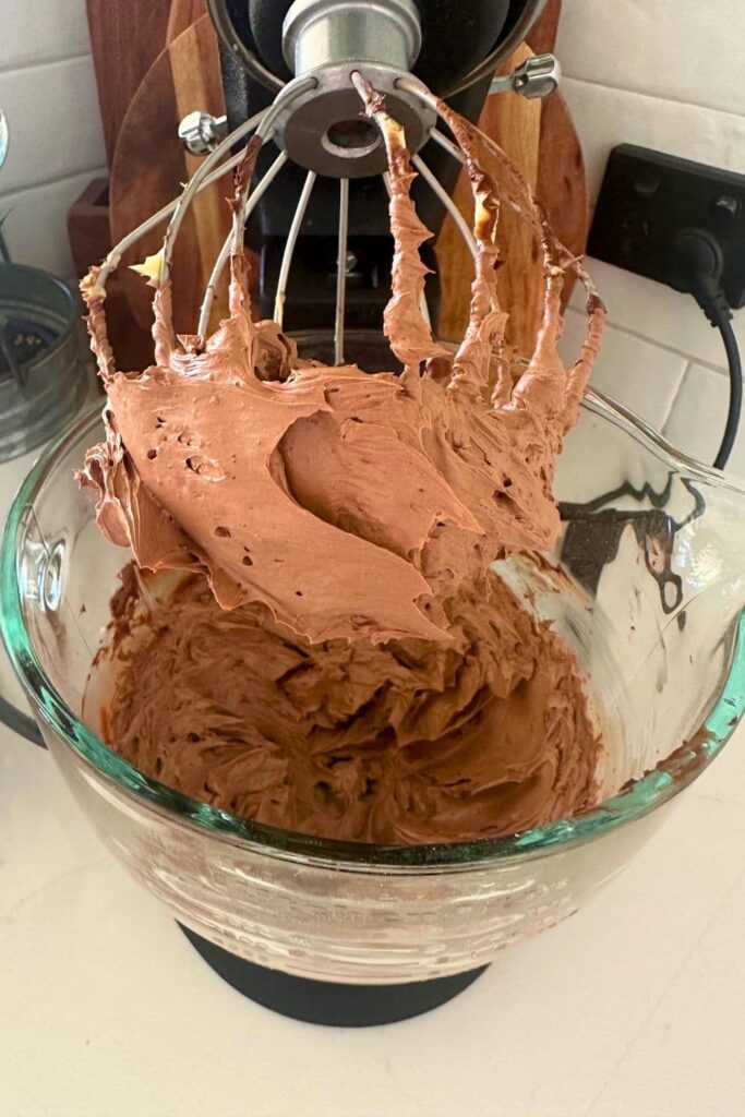 Rich whipped chocolate butter on the whisk of a Kitchen Aid stand mixer that has been lifted out of the bowl.