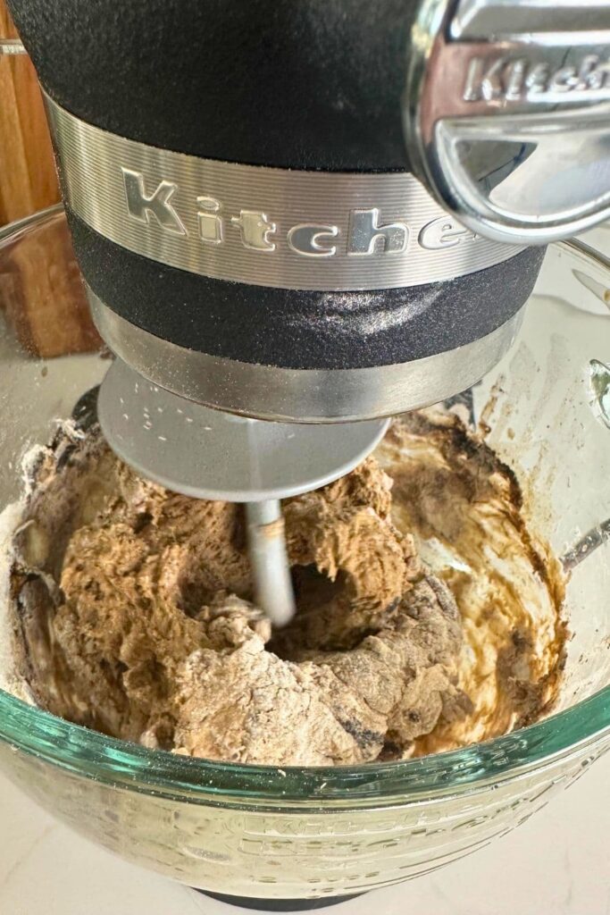 A glass KitchenAid bowl filled with the shaggy dough that is being mixed to make sourdough brown bread.