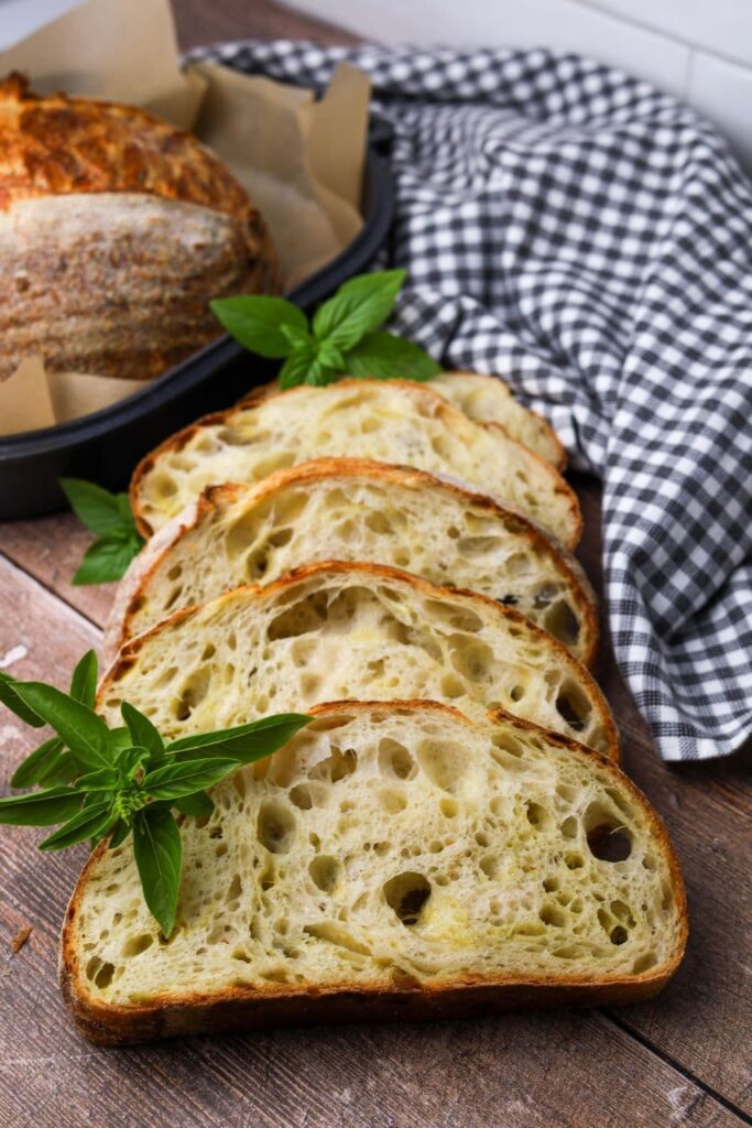 4 slices of sourdough mozzarella pesto bread laid out on a wooden table. You can see the rest of the loaf sitting in the background of the photo. The loaf is garnished with fresh basil leaves.
