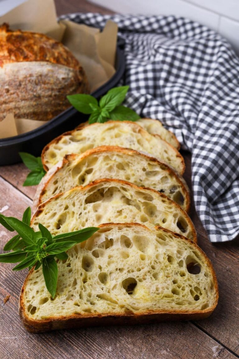 4 slices of sourdough mozzarella pesto bread laid out on a wooden table. You can see the rest of the loaf sitting in the background of the photo. The loaf is garnished with fresh basil leaves.
