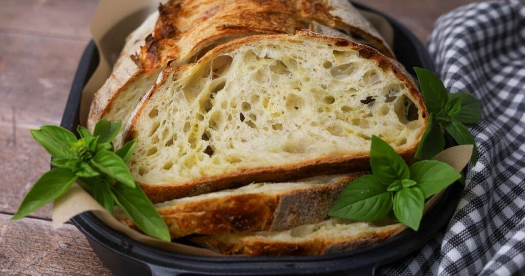 A slice of pesto mozzarella sourdough bread laid in a cast iron bread pan. The bread is surrounded by fresh basil leaves.