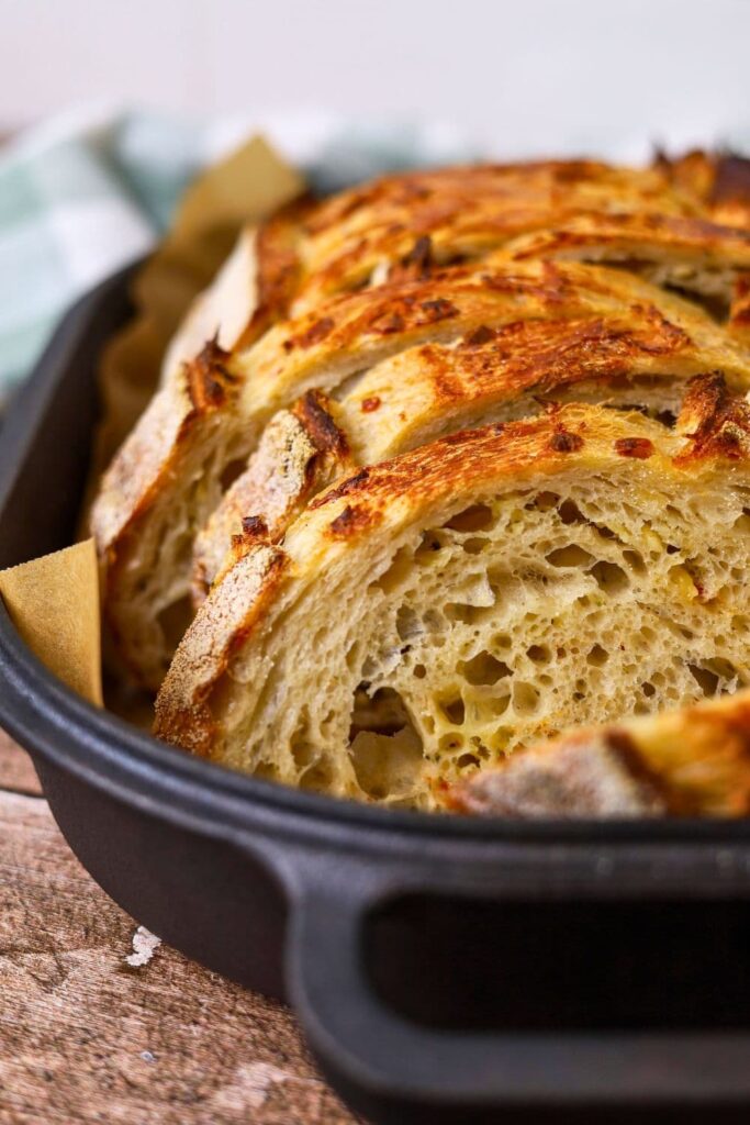 Close up photo of a loaf of Italian herb and cheese sourdough bread that has been sliced.