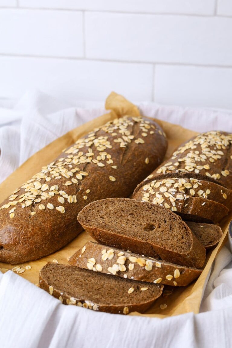 2 loaves of sourdough brown bread topped with rolled oats. One loaf has been sliced up and the other has been left whole.