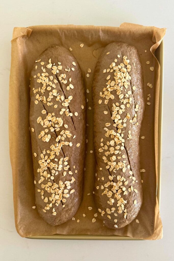 Two loaves of sourdough brown bread sprinkled with rolled oats ready to be baked in the oven.