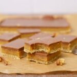 Squares of sourdough caramel slice stacked on top of each other. The top slice has a bite taken out of it.