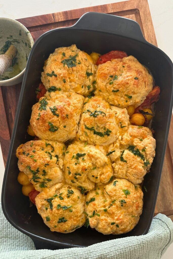 Sourdough tomato cobbler that has been baked until golden brown and topped with garlic and herb butter.