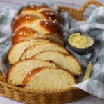 A loaf of sweet braided sourdough bread that has been sliced up and displayed in a basket next to a small dish of butter.