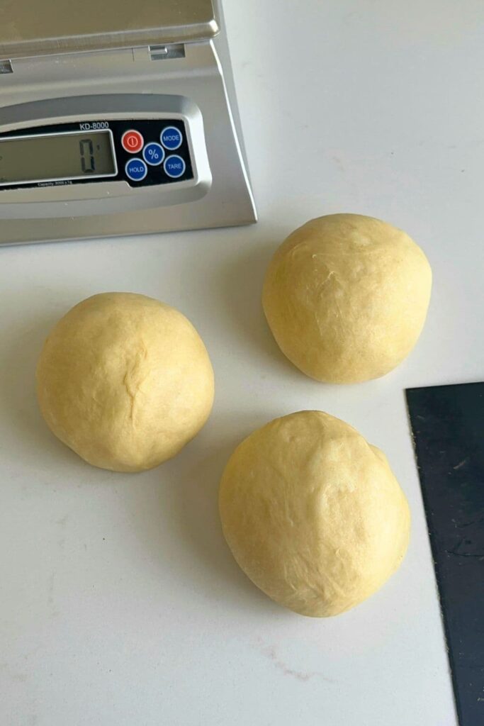 Three balls of sweet sourdough sitting on a counter top next to a digital kitchen scale.